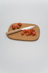 datterini tomatoes and knife on a wooden chopping board on a blank white background