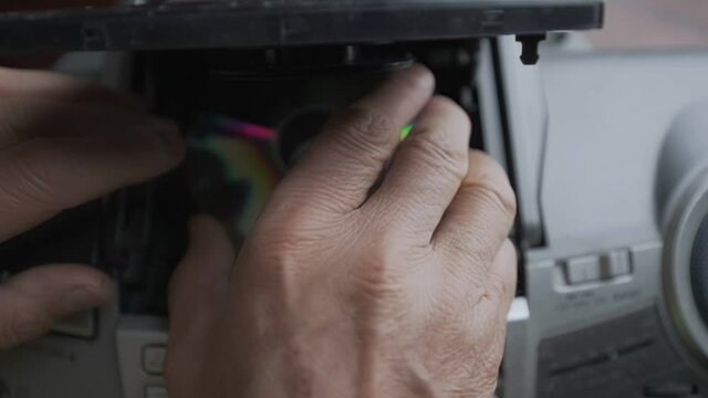 Older man with wrinkled hand changing CD disk in retro music boombox top view. Vintage audio and stereo equipment collection.