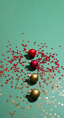 Top view of four Christmas festive decoration gold and red toy balls with sequins glitter on a mint green background.