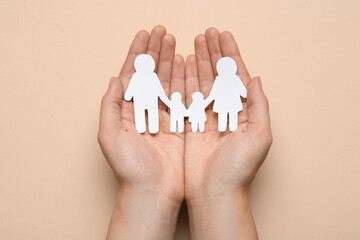 Woman holding paper family cutout on beige background, top view