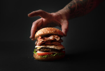 Mano tocando delicadamente hamburguesa doble con tocino y carne, reci&eacute;n horneada.