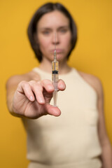 Serious Caucasian woman holds a syringe filled with liquid in her hand. Concept of drug addiction or covid-19 vaccination. 