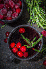 Autumn winter cranberry tea with rosemary and orange slices, dark concrete background copy space