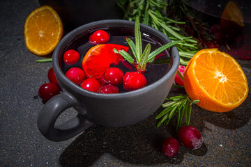 Autumn winter cranberry tea with rosemary and orange slices, dark concrete background copy space