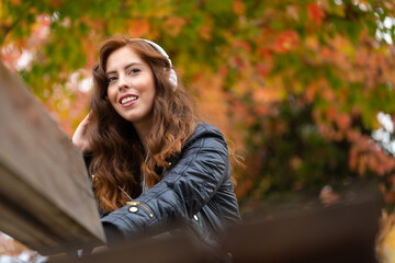 Fototapeta na wymiar Girl listening to music with white headphones on a park bench in autumn