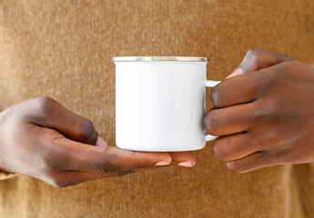 Camp metal enamel mug mockup. Close up african-american hands holding white cup with stainless steel ring, copy space. Front view, space for branding imprint