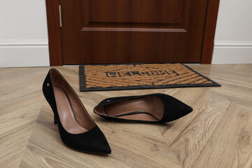 Stylish female shoes near door mat in hall