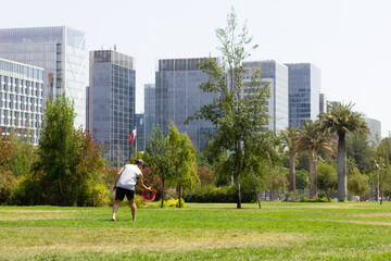 Young man playing with flying ring on sunny day at the park and financial buildings on background....
