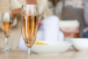 Glasses of sparkling rose wine and snacks on table and blurred women on background. Friends meeting, party celebration concepts
