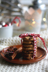 Stack of chocolate chip cookies tied with ribbon, cinnamon, anise, various Christmas decorations and lit candles. Hygge at home. Selective focus.