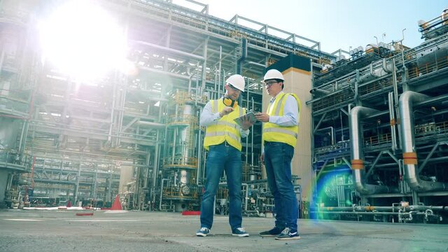 Male partners are talking next to the refinery pipelines