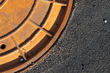 Rusty red sewer manhole in a tarmac road, close-up
