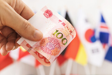 One hundred yuan in hand against the background of flags of different countries, close-up