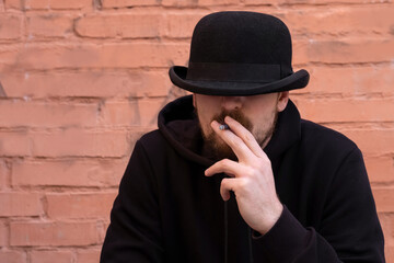 Man in black smokes a cigarette on a wall background.