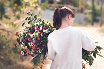 The girl carries a huge bouquet of flowers on a sunny day. back view.