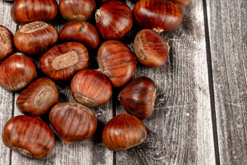 some raw chestnuts, marron (Castanea sativa), a classic autumn fruit, on light colored wooden rustic background.