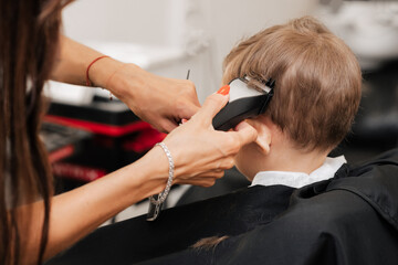 Shooting in a beauty salon. A barber cuts the hair of a little boy with a machine.