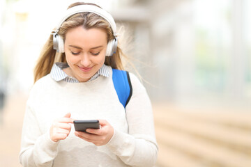 Happy student listening audio with headphones in the street
