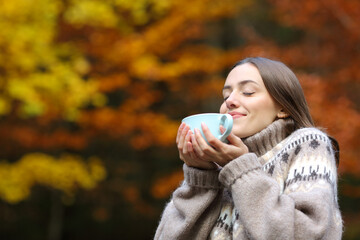 Happy woman in autumn smelling coffee in a park