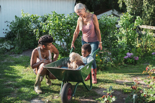 Woman looking at son sitting with dog in wheelbarrow held by mother