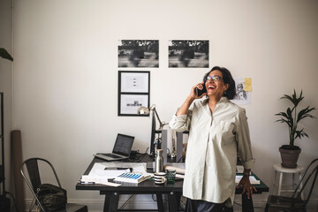 Senior craftswoman laughing while talking on mobile phone in office