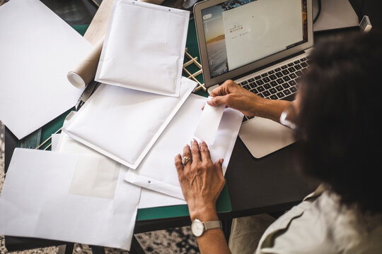 High angle view of female owner labeling on envelope while working in office