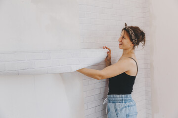 Young woman glues wallpaper at home. girl glues wallpaper in the form of a brick. repair.