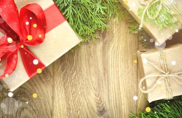 Christmas photo with wrapped gifts tied with red ribbons on a wooden background. Gold highlights on a green fir background with copy space.