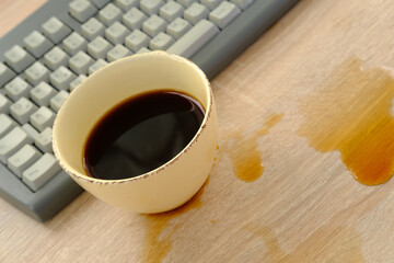 closeup of computer keyboard, cup of coffee, tea suddenly spills, hot liquid spoils equipment,...