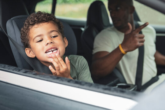 Playful boy showing broken teeth while sitting by father in electric car