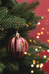 Christmas concept with trendy red decoration hanging on a fir tree. New Year ornament with golden bokeh.