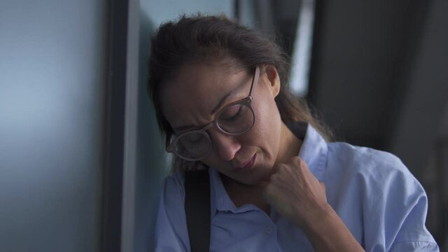Attractive multiethnic woman in eyeglasses leaning head on wall, feeling sickness and dizziness, symptoms of pregnancy, low blood pressure, overworking and exhaustion, queasiness, sadness