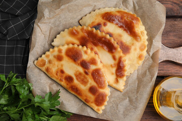 Board with delicious fried chebureki and parsley on wooden table, flat lay