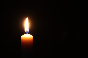 Flame of one candle on a horizontal black background Candle on the left side of the photo with free space for text on the right