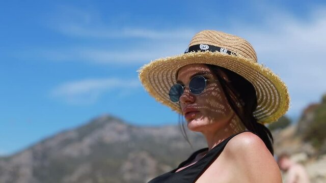 Pretty slim woman in bikini and straw floppy hat walking lies the beach and enjoying summer heat. Vacation concept