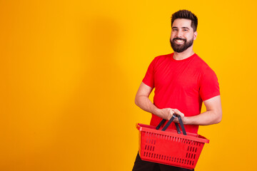 handsome caucasian boy holding a shopping basket on yellow background. shopping concept