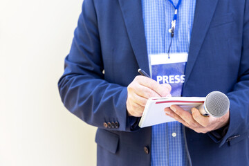 Journalist with press pass at news conference or media event, holding microphone, writing notes