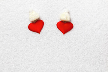 Fototapeta premium Two red hearts in white knitted hats on the snow.