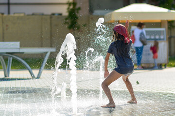 A girl is dancing in a fountain in a park on a hot summer day.