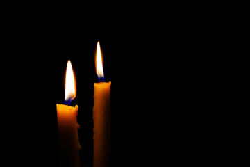 Two burning candles in the darkness. Burning yellow candles on black background with copy space.