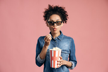 Astonished young female in 3d glasses watching interesting movie film, holding and eating popcorn