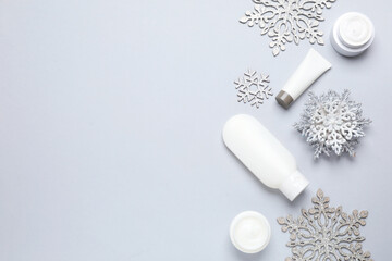 Flat lay composition with cosmetic products and snowflakes on light grey background, space for text. Winter skin care
