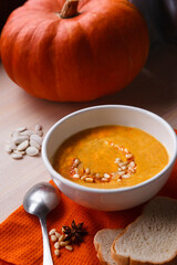 Homemade pumpkin soup with fresh pumpkin and bright orange kitchen cloth on white table