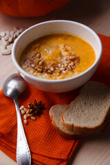 Homemade pumpkin soup with fresh pumpkin and bright orange kitchen cloth on white table