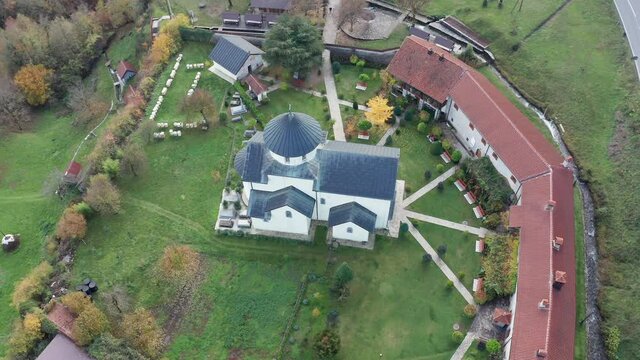 White Christian church surrounded by monastery buildings on a green field. Aerial drone view of Moraca orthodox monastery in Montenegro Europe.