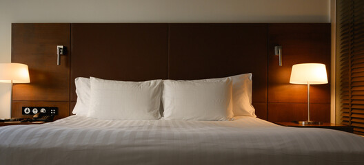 Front view of double bed in hotel near lamp or lantern glowing on nightstand in modern bedroom...