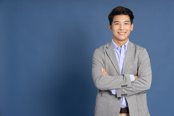 Smiling young Asian businessman with arms crossed in blue studio isolated background - Powered by Adobe