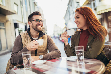 Attractive young couple in love sitting at the cafe table outdoors, drinking coffee