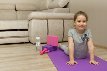 Smiling little girl doing fitness, yoga, sports at home. She lies on the yoga mat, propped up in her arms.