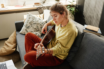 Young woman enjoying playing guitar on the sofa in the living room at home